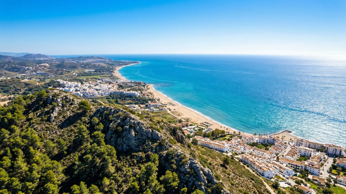 Luftfoto af Costa del Sols kystlinje med livlige middelhavsfarvande, sandstrande og Sierra de Mijas-bjergene under en klar blå himmel.