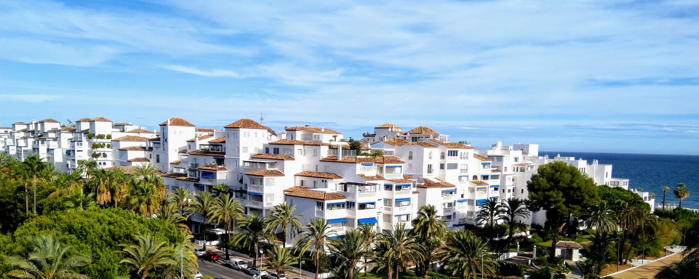 Aerial panoramic view of white Andalusian-style residential apartments amid palm trees with Mediterranean Sea backdrop, Puerto Banús / Nueva Andalucía, Costa del Sol, shown as local context near VILLA LAS PALOMAS