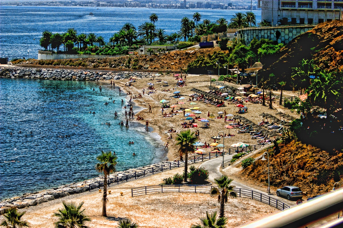 ABELIAS area photograph of the Benalmádena Costa beach cove, with the Mediterranean Sea, palm-lined promenade and sunbathers seen from an elevated position