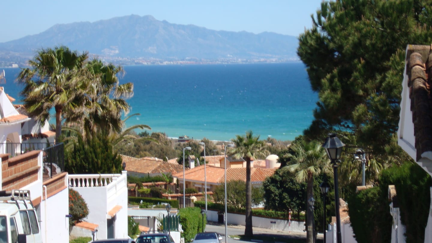 MORASOL - BUILDING 2: elevated coastal view over the Manilva residential area towards the Mediterranean Sea, with palm trees and mountains in the background