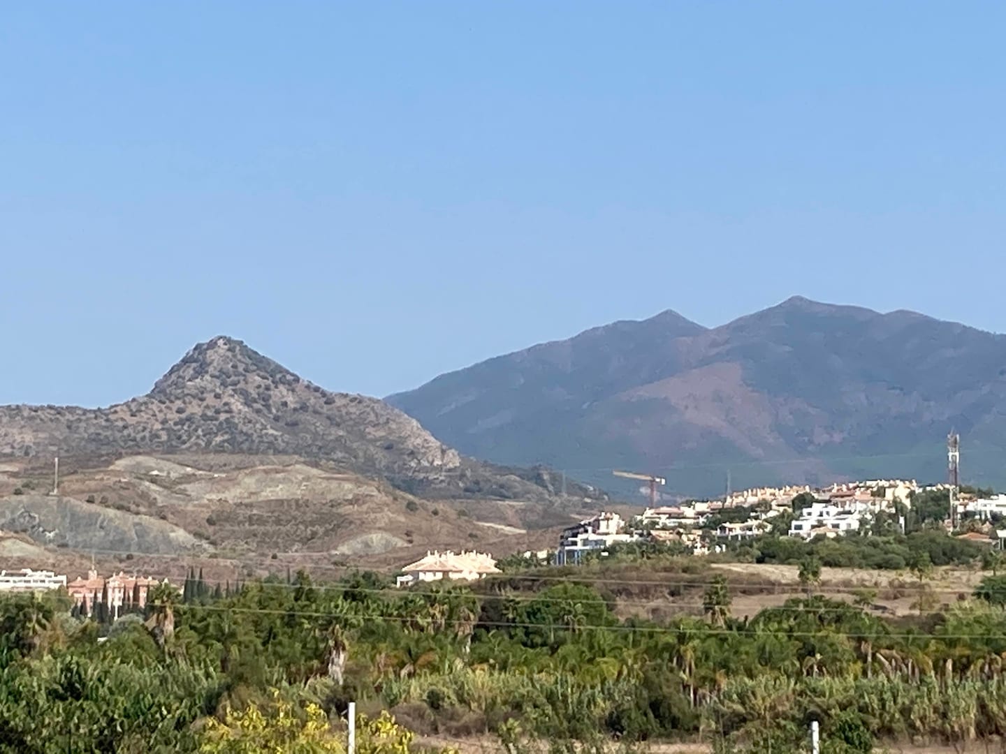 Mountain landscape near Estepona, with Sierra Bermeja foothills, subtropical agricultural foreground and distant low-density residential development, shown as local context near VILLA ESMERALDA