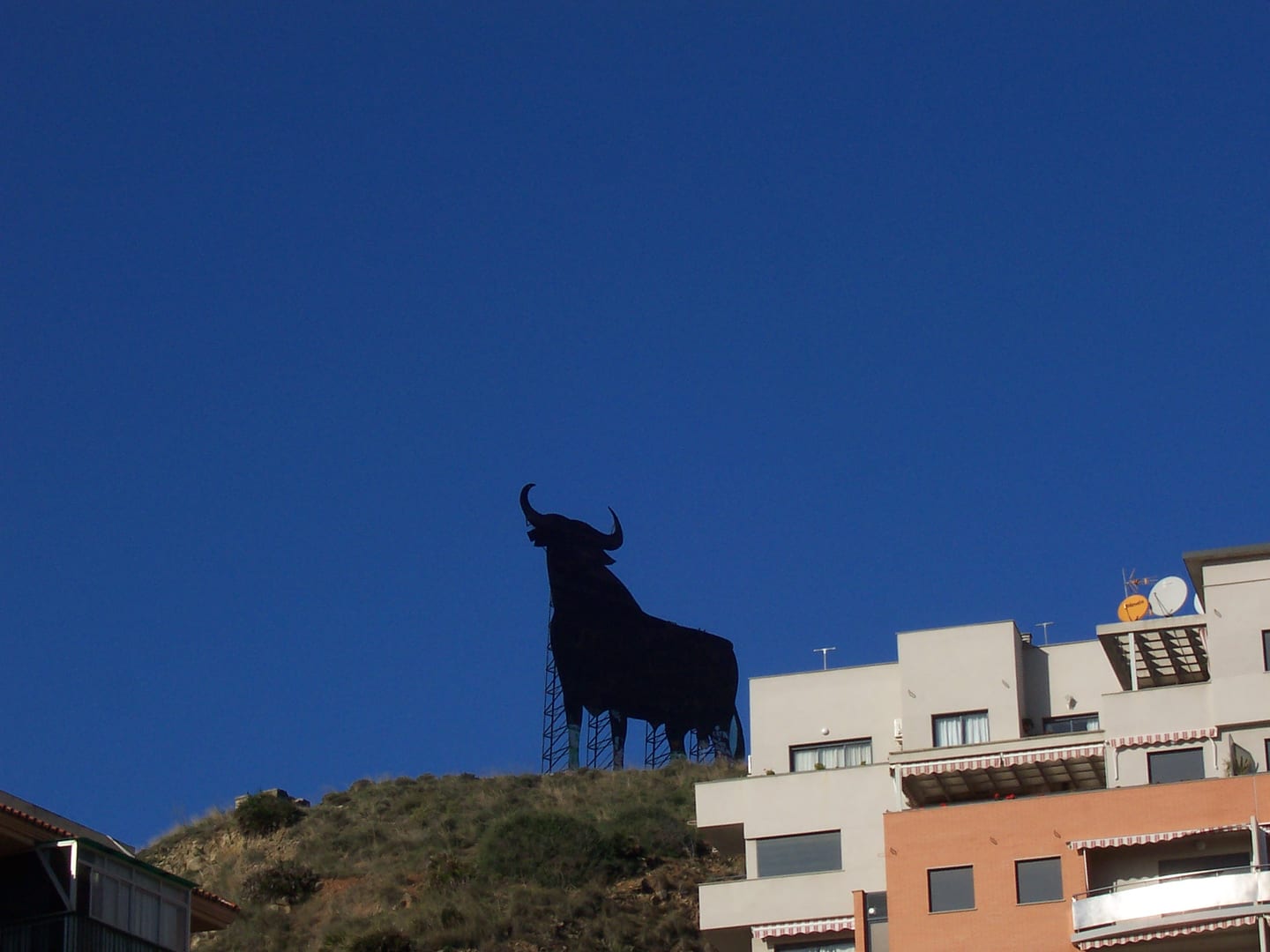 TORRE BIZNAGA area photograph of the Osborne bull landmark on the hillside above Fuengirola, with residential buildings and clear blue sky