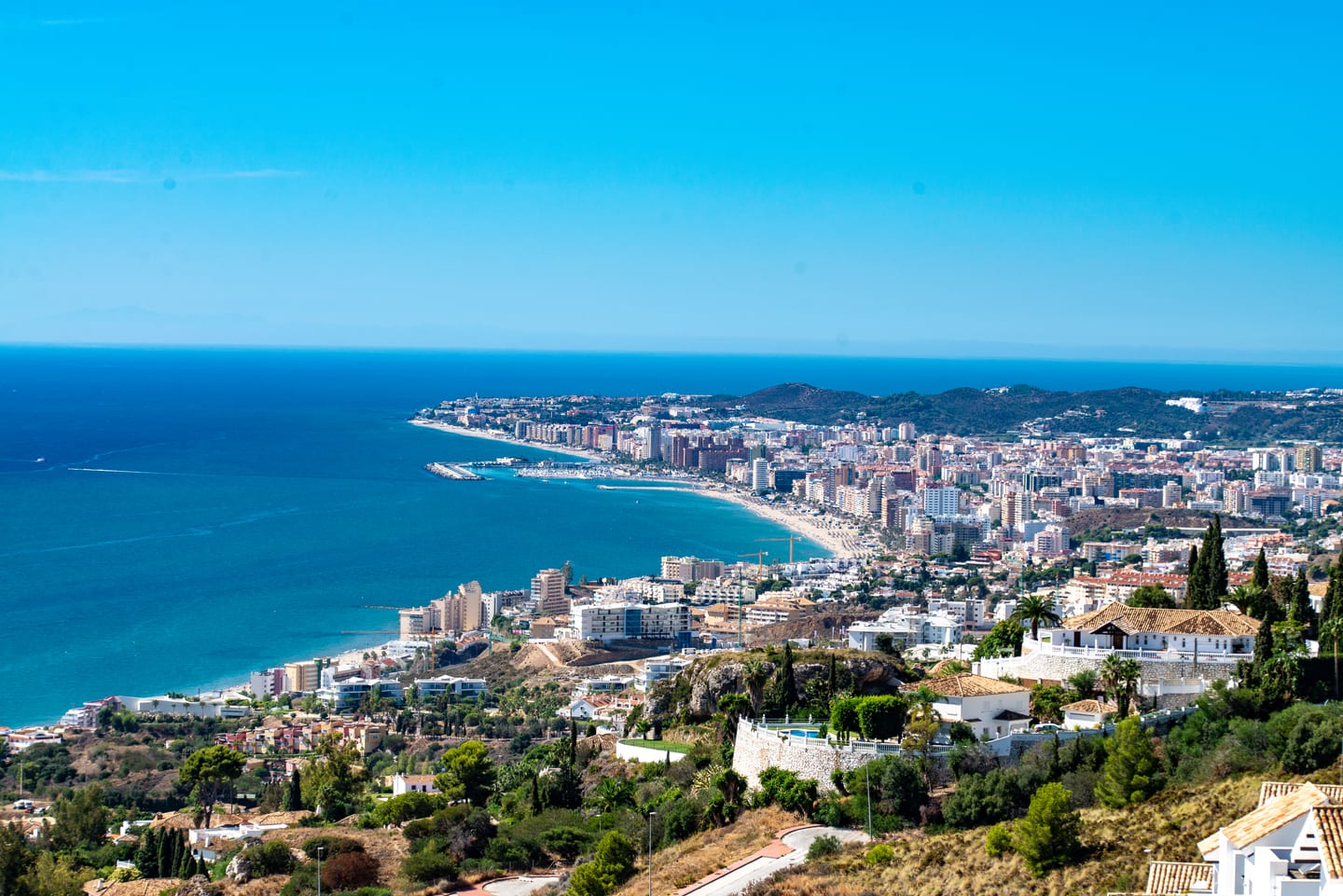 Panoramic coastal view of Fuengirola near CORE HIGUERON FASE II, showing the beach, marina, urban shoreline and Mediterranean Sea, with residential villas in the foreground.