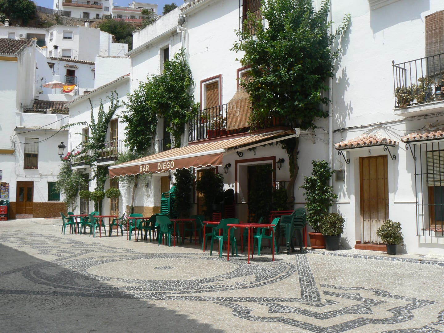 CALLE MIRÓ: traditional whitewashed village square (plaza) in Ojén with mosaic cobblestone paving and a bar terrace, Andalusia, Spain