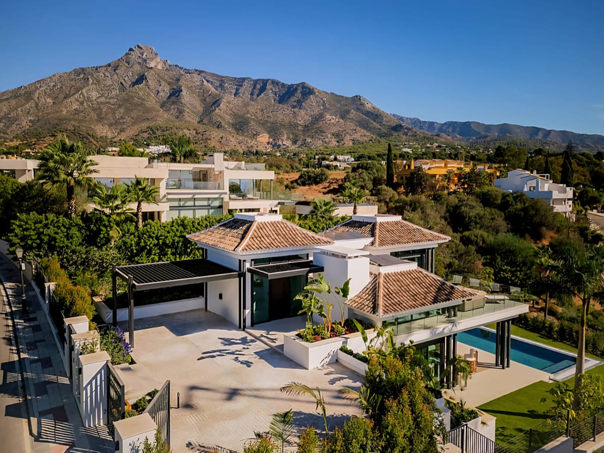 Aerial project image of 4OUR VILLAS with tiled roofs, a covered carport at the entrance, a rectangular swimming pool on the right and a prominent mountain in the background.