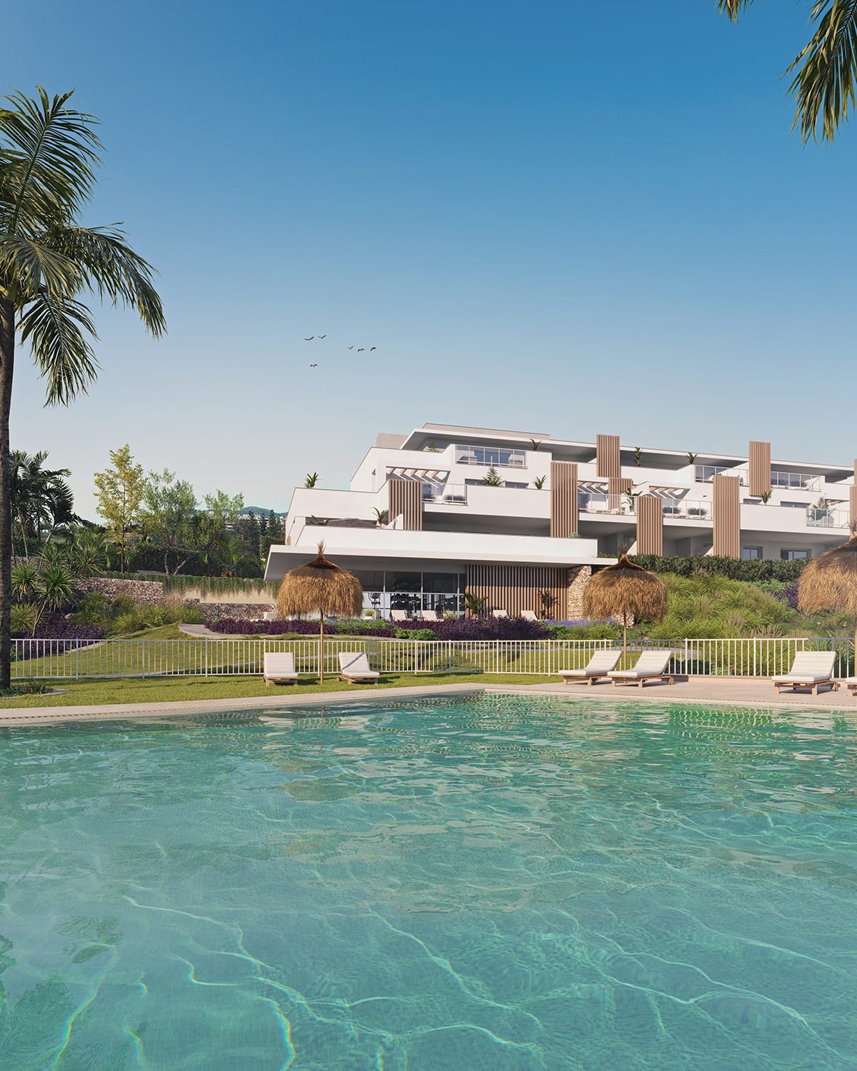 Project visualisation of ABRIL DOÑA JULIA viewed from the pool: turquoise water in the foreground, sun loungers and thatched dome parasols behind a white fence, and a white façade with vertical wooden elements against a green hillside backdrop.