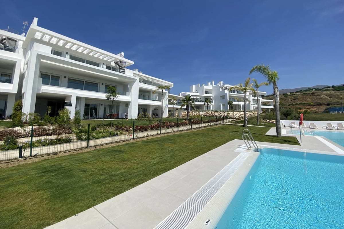 ALCAZABA LAGOON IV with a blue swimming pool in the foreground, a lawn, palm trees and white buildings with terraces in the background.