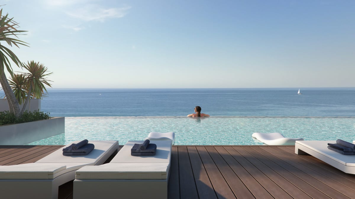 Project visualisation of ARRECIFE featuring an infinity pool, wooden deck, white sun loungers with dark towels and sea views with a sailing boat on the horizon.