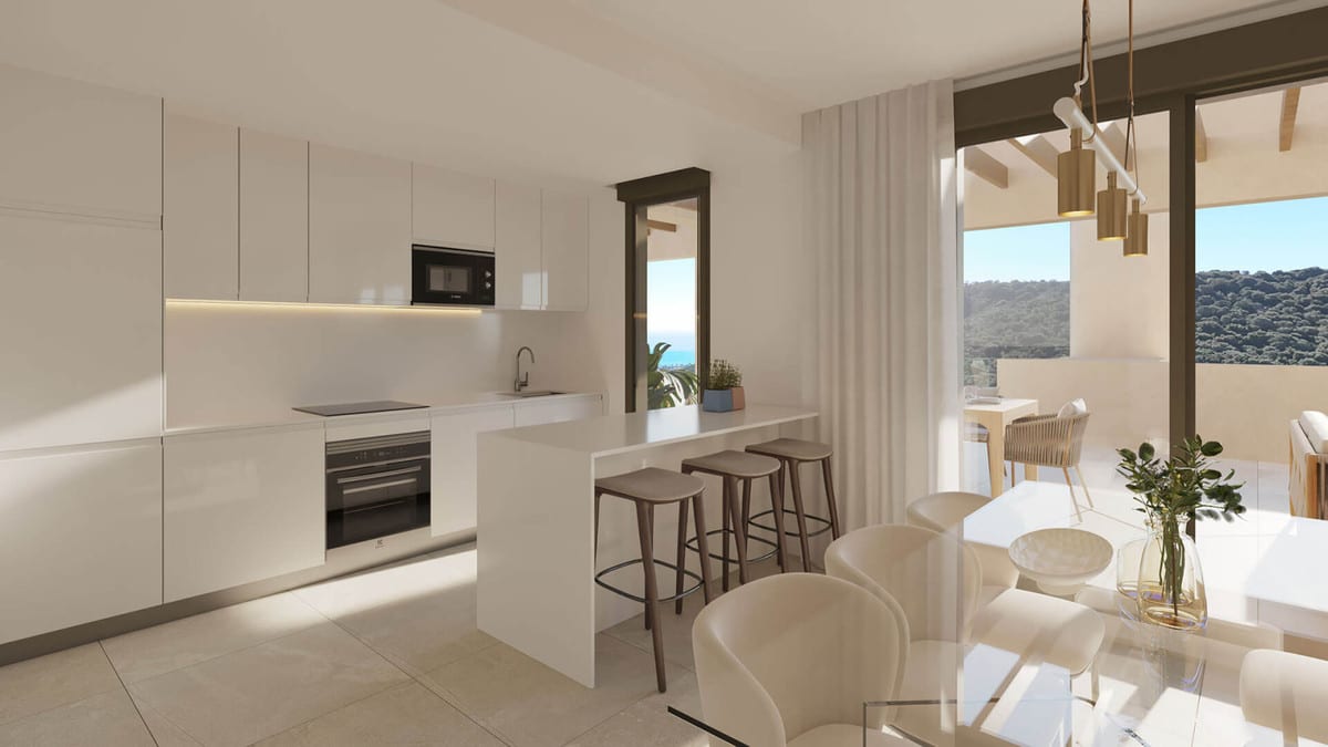 Rendered interior visualisation of ATRIA - PHASE 1 with a white kitchen, kitchen island with bar stools, light dining table with chairs and sliding doors leading to a terrace with sea views and a hilly landscape.