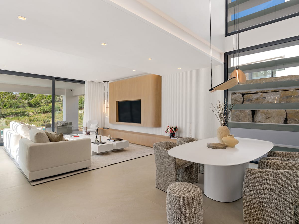 Living and dining area with cream seating, an oval table and a TV wall with a wood-effect finish.