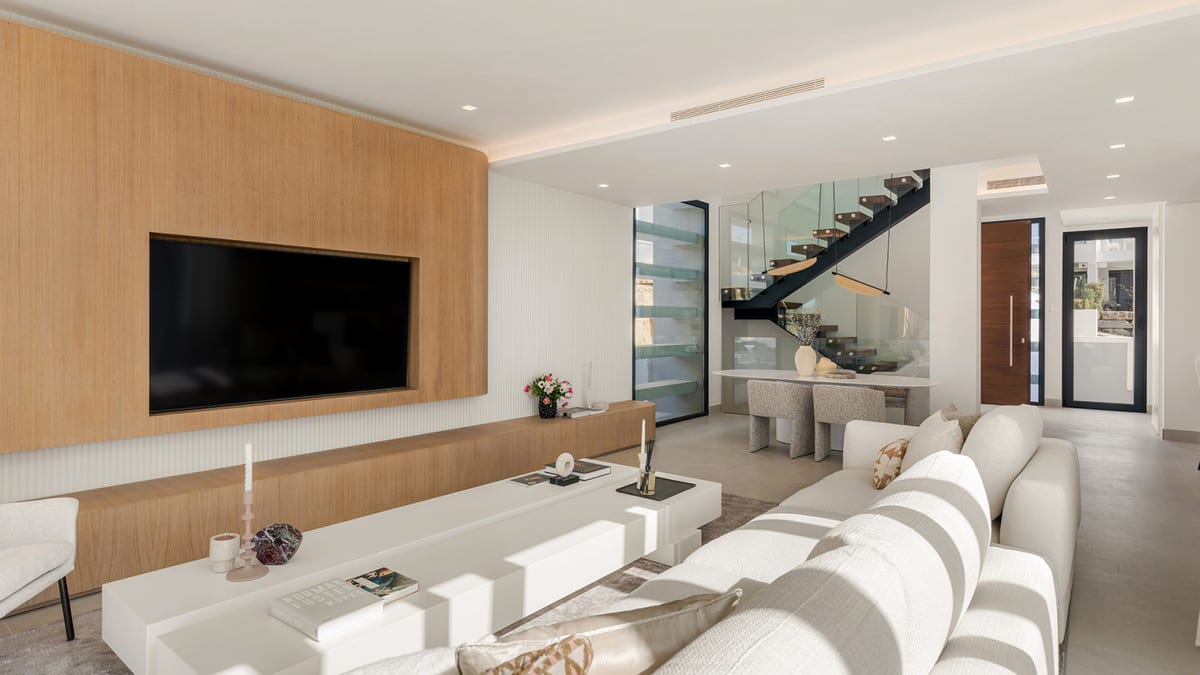 Living room overlooking the dining area and staircase with glass balustrade and dark handrail.
