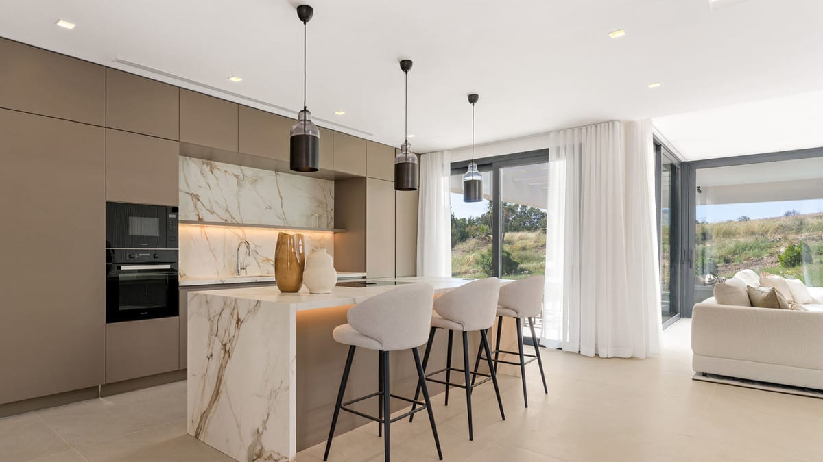 Kitchen with taupe cabinets, a marble-effect island, three light bar stools and pendant lights.