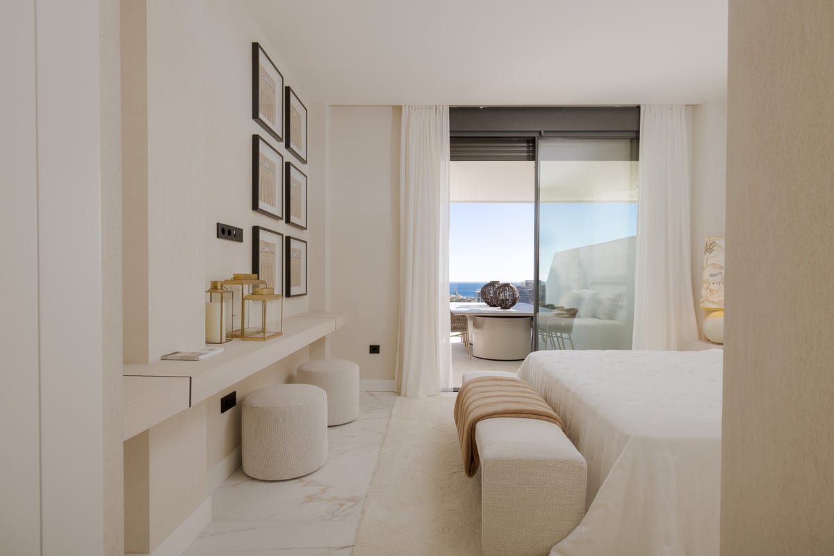Light bedroom with a wall shelf, round stools and sliding glass doors towards the terrace and sea.