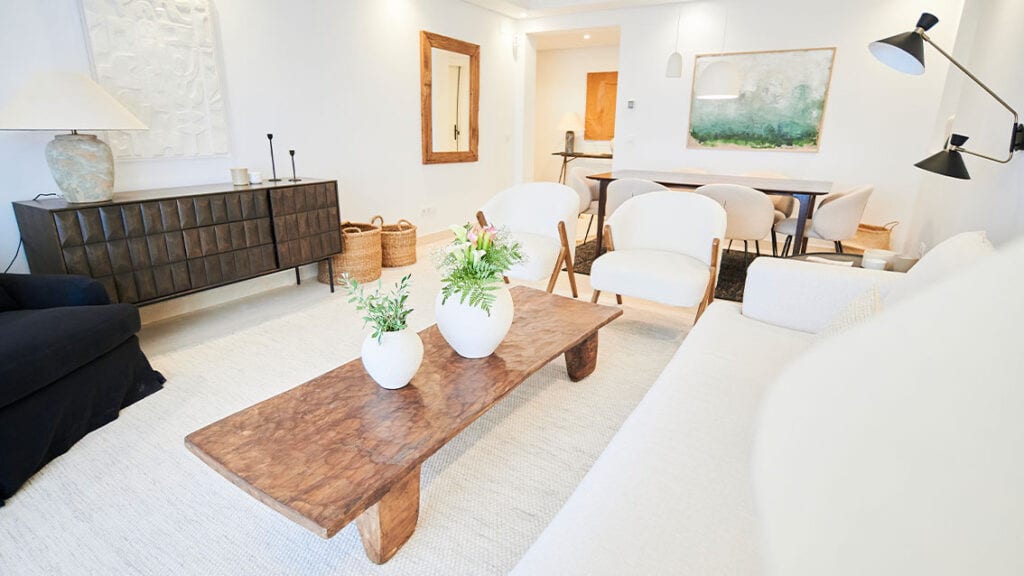 BE ALOHA living room with white sofa, wooden coffee table with vases, dark-brown wooden cabinet and dining area with light-coloured chairs