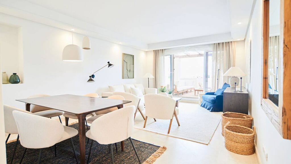 BE ALOHA open-plan living and dining area with dark wooden dining table, light-coloured chairs, white seating area and glass doors with natural light