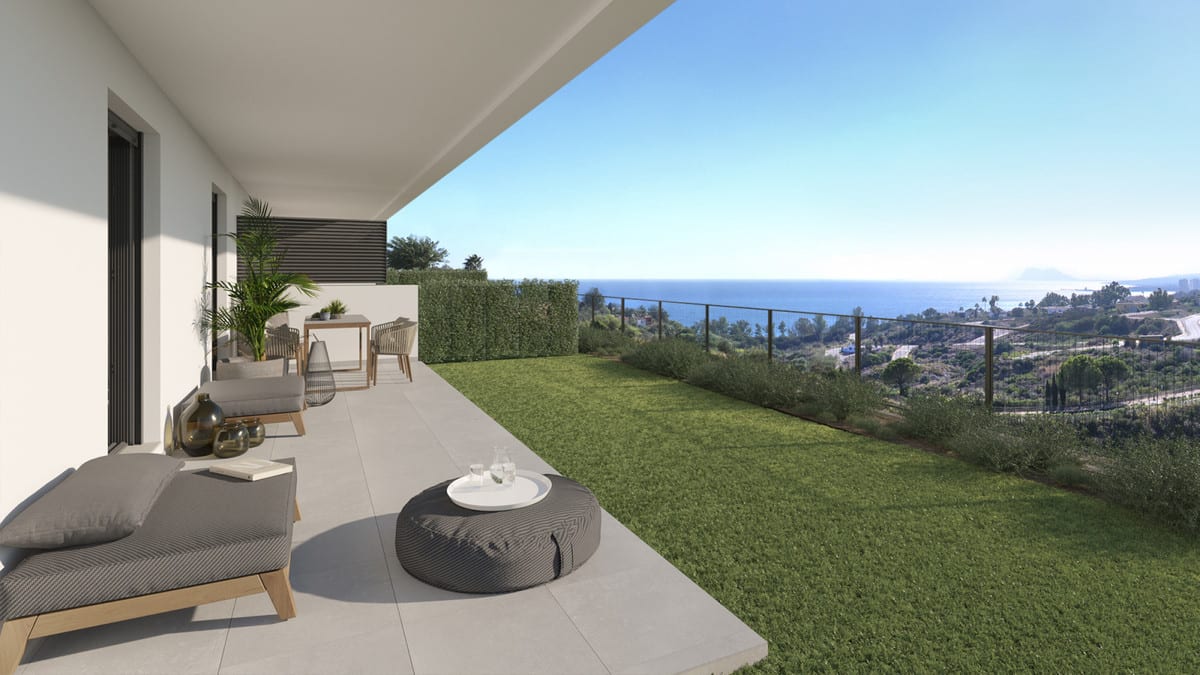 Rendered project visualisation of BLUE VIEW HEIGHTS with a covered terrace, sun lounger, round pouffe, small seating area with table and chairs, adjoining lawn and cable balustrade, with the sea visible on the horizon.
