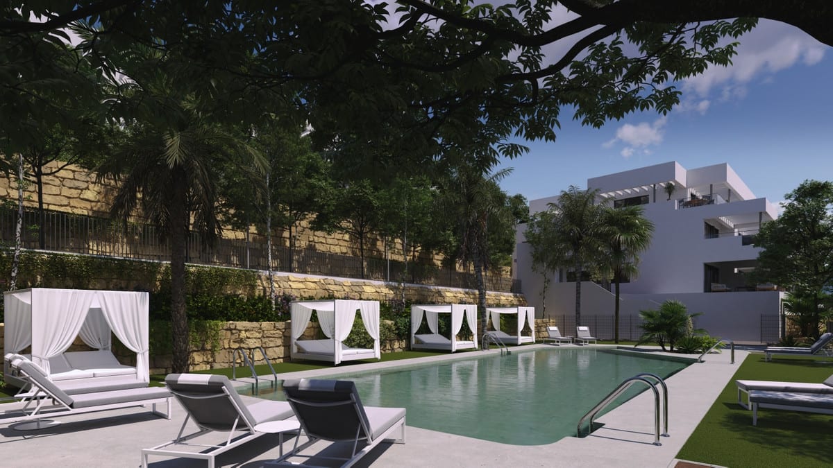 Project visualisation of the pool area at CAMARATE HILLS II with sun loungers, white daybeds, palms, a lawn, a stone retaining wall and a white building in the background.