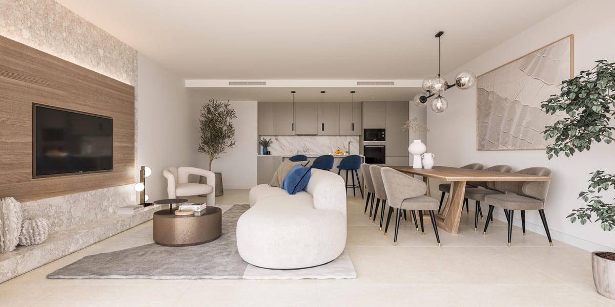 Project visualisation of CAPRI - FASE 2 featuring an open-plan living space with a curved white sofa, round bronze coffee table, white armchair, wooden TV wall with a stone accent, long dining table with taupe chairs, and an open kitchen with a marble splashback in the background.