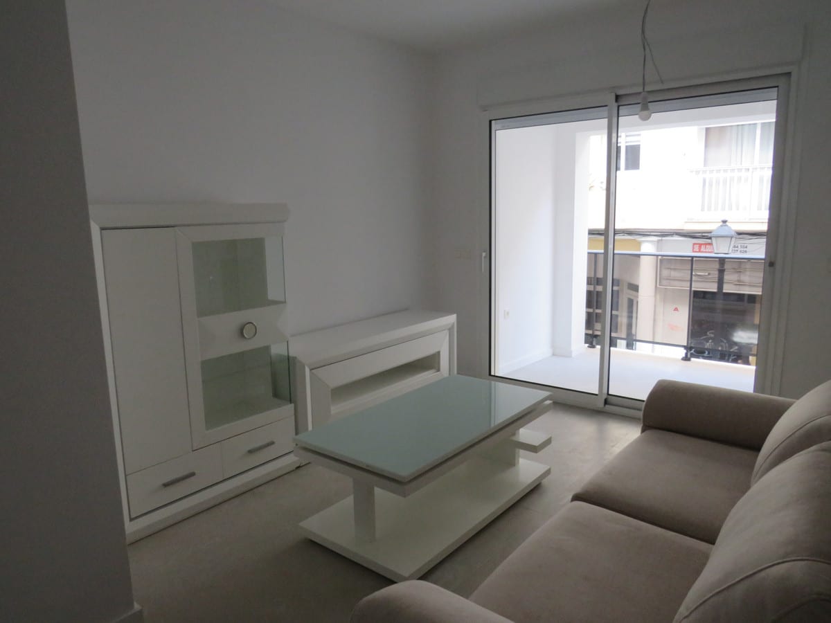 Living room at EDIFICIO VENECIA with a beige sofa, white display cabinet, glass coffee table and sliding doors leading to an outdoor area.