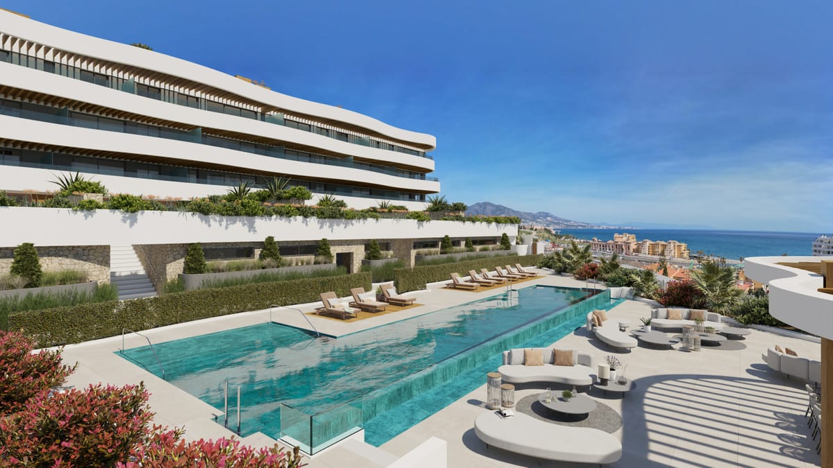 Project visualisation of ELYSEA SUITES with a white modern building, a rectangular outdoor swimming pool, sun loungers, planting and the sea in the background.