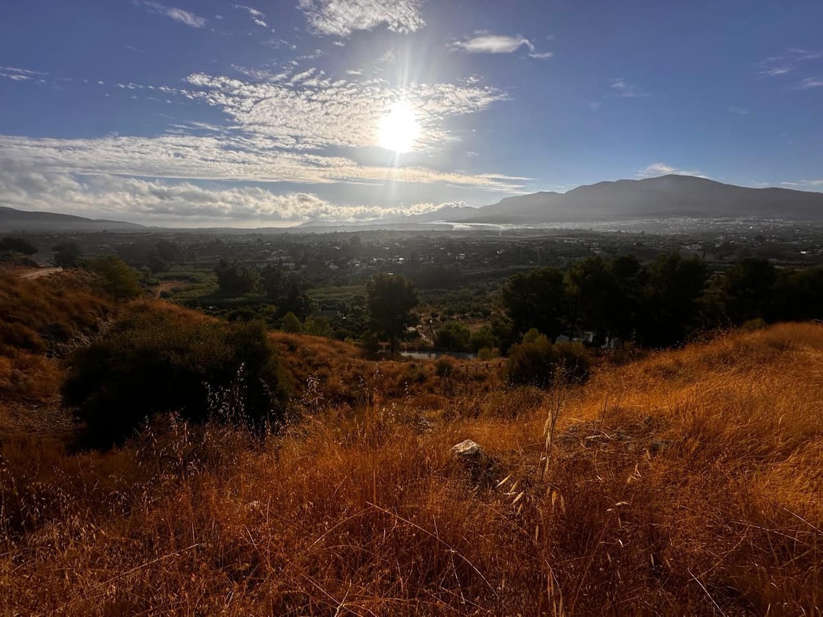 Landscape photograph with dry grass, scattered buildings in the valley and mountains beyond.