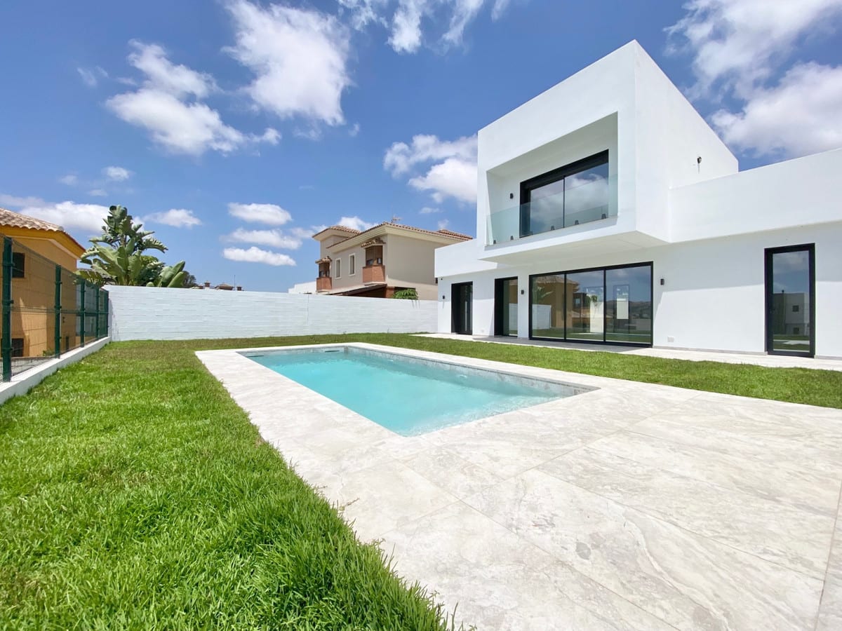 Corner view of the garden with a pool, light paved terrace and broad sliding glass doors.