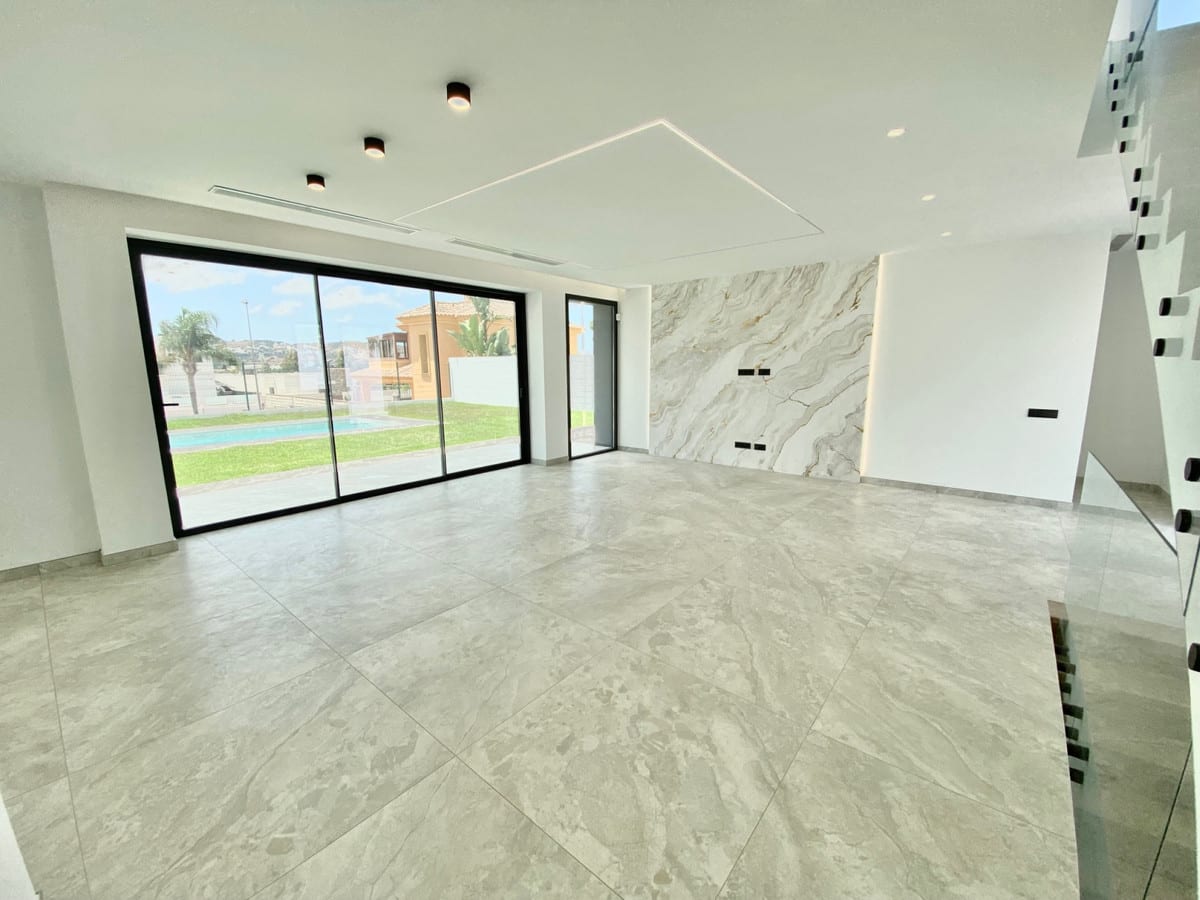 Unfurnished living space with a glass stair balustrade, grey floor tiles and garden views through sliding doors.