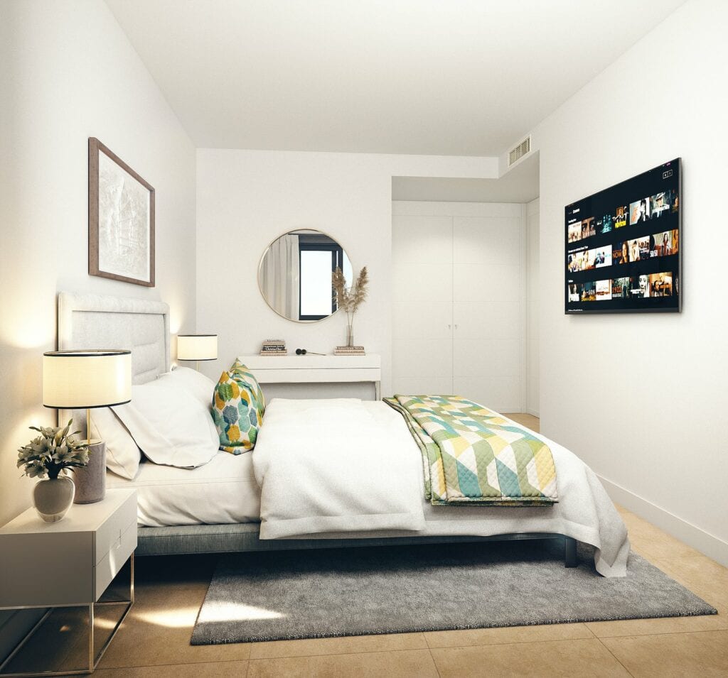 Project visualisation of a bedroom in HABITAT ALBORÁN - BORA with a double bed, bedside table, dressing table with a round mirror, wall-mounted television and white fitted wardrobe.