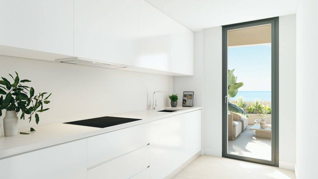 Project visualisation of a white kitchen in HABITAT ALBORÁN - BORA with ceramic hob, sink, extractor hood, handleless cabinets and an aluminium door leading to a terrace with plants and water visible in the background.