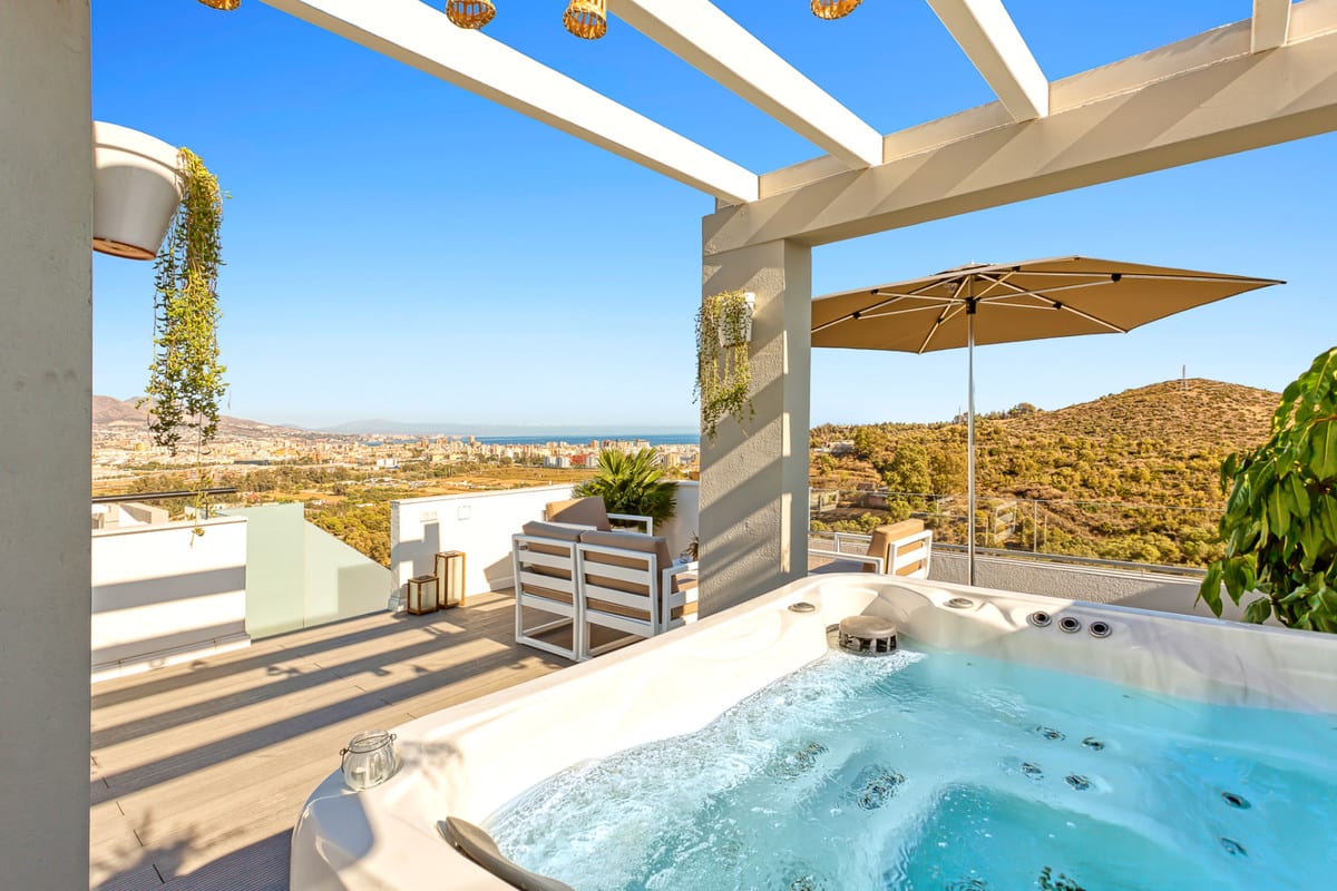 HACIENDA EL SUEÑO with an active hot tub on a terrace beneath white pergola beams, seating, a parasol and views of hills and buildings in the distance.