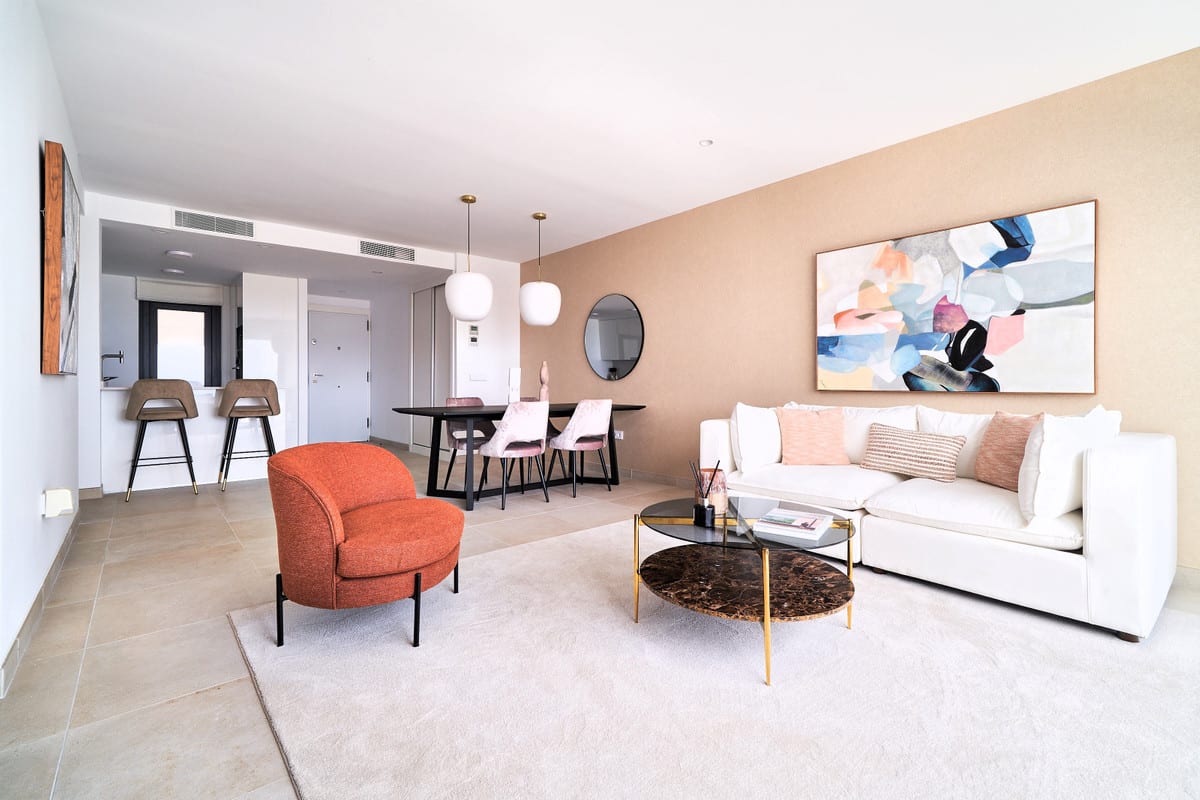 HIGUERÓN BAY RESIDENCES with a white sofa, terracotta armchair, dark coffee tables with marble-effect tops, a black dining table with pink chairs, bar stools at the kitchen island and colourful wall art.
