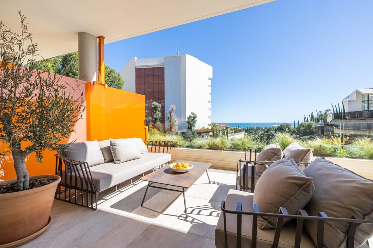 View of a terrace seating area with sofas, a low table, a potted tree and an orange wall.