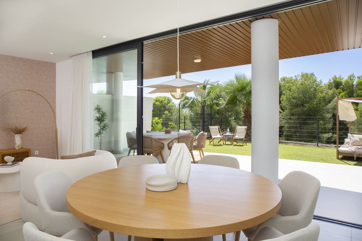HIGUERON WEST with a round wooden dining table indoors and a covered terrace leading to a garden.