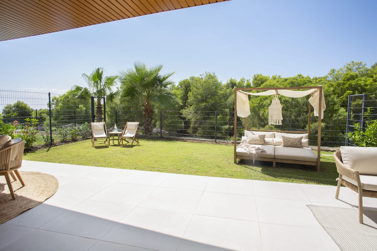HIGUERON WEST with a light-tiled terrace, lawn, two folding chairs and a wooden daybed with macramé decoration.