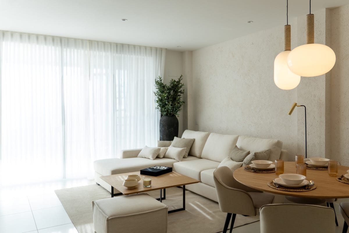 HORIZON36 woonkamer met crèmekleurige hoekbank, vierkante houten salontafel, ronde eettafel met gestoffeerde stoelen, bolvormige hanglampen en witte vloergordijnen.