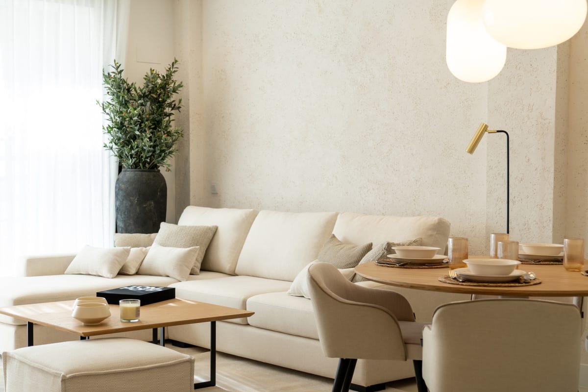 HORIZON36 zithoek met crèmekleurige bank, sierkussens, vierkante houten salontafel, ronde eettafel met gedekte borden en een zwarte vloerlamp met gouden kap.