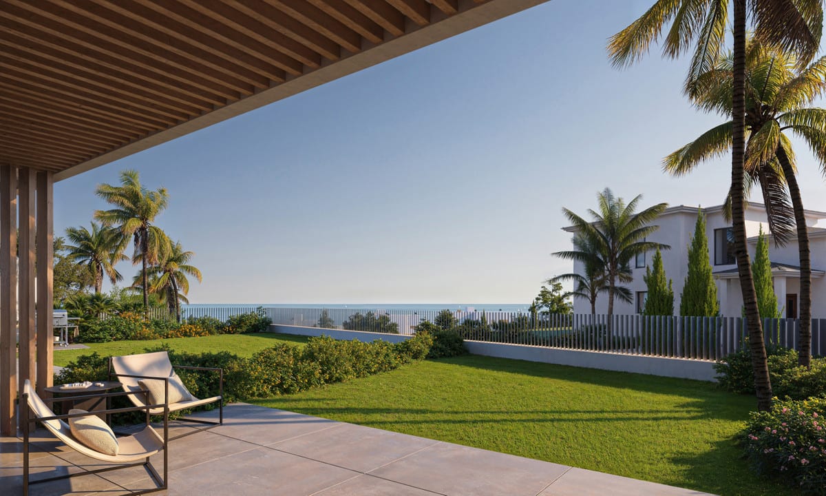 Project visualisation of HORIZONTE VILLAGE - THE RESIDENCES featuring a covered terrace with a wooden slatted ceiling, two lounge chairs, a lawn with palm trees and the sea on the horizon.