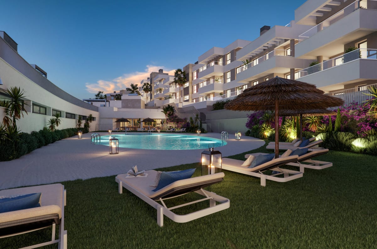 Evening visualisation of INSUR SCALA with an illuminated oval swimming pool, white sun loungers, a large thatched parasol, lanterns on the grass and lush flowering planting.