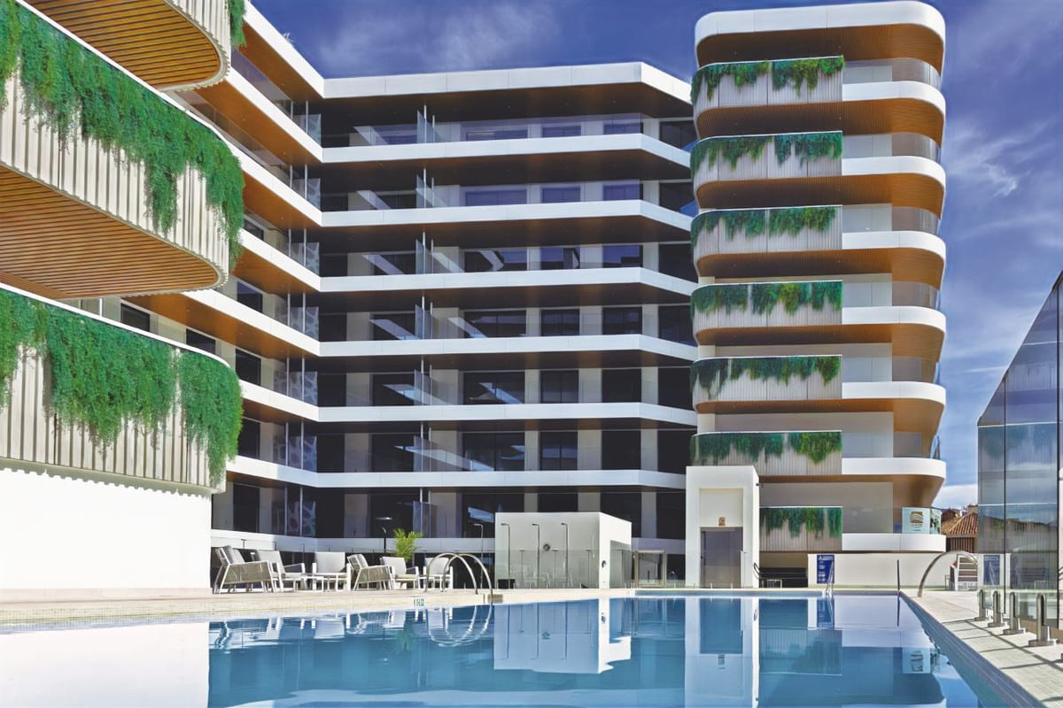 Rendered project visualisation of JADE TOWER with an outdoor swimming pool in the foreground, multiple floors with glass balustrades, white façade bands, wooden balcony decking and hanging greenery on the façades.
