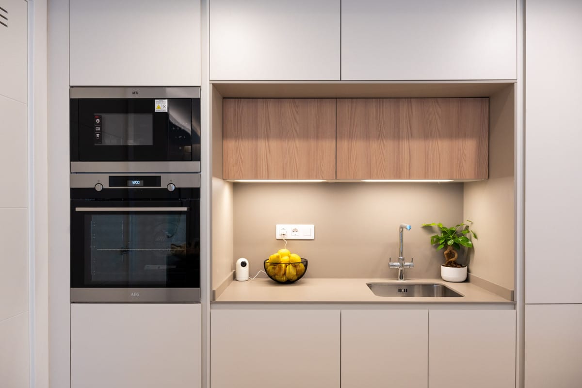 Kitchen at JADE TOWER with light-grey matt-white cabinets, wooden upper cabinets in a recess, built-in AEG microwave and AEG oven, and a stainless-steel sink with tap.