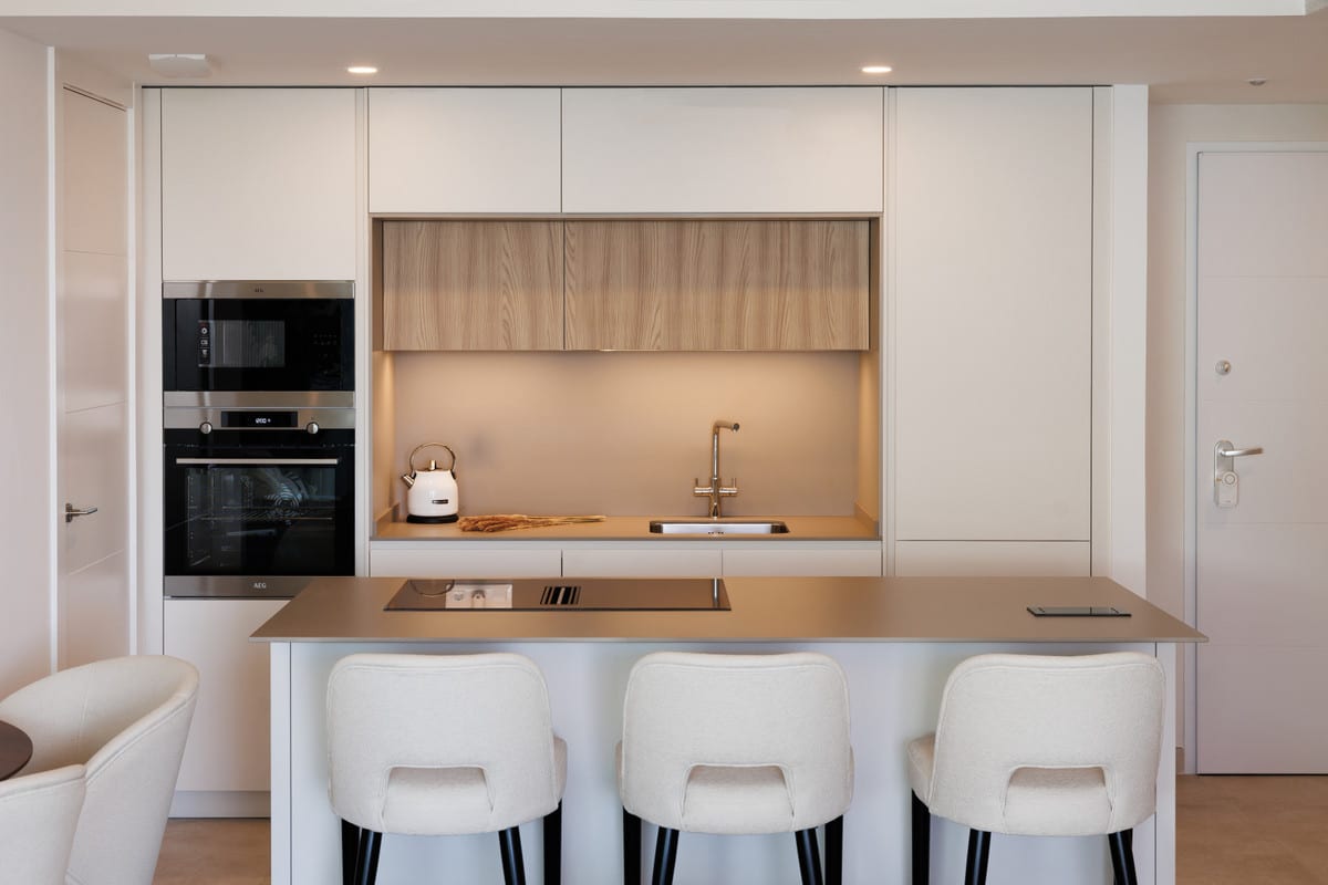 JADE TOWER WITH FURNITURE with a white kitchen, wooden upper panels, kitchen island and three upholstered bar stools.