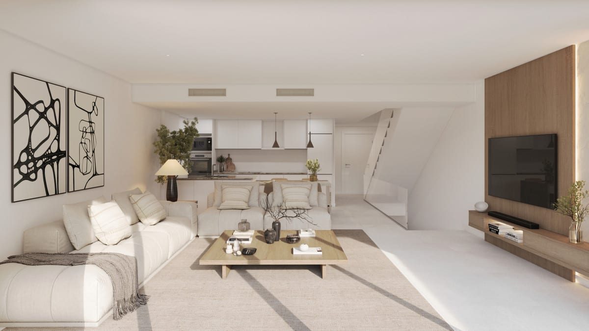 Rendered living room at KALA RESIDENCES with a large light-coloured sofa, wooden coffee table on a rug, open-plan kitchen with pendant lights, white staircase and wooden TV wall with a mounted television.