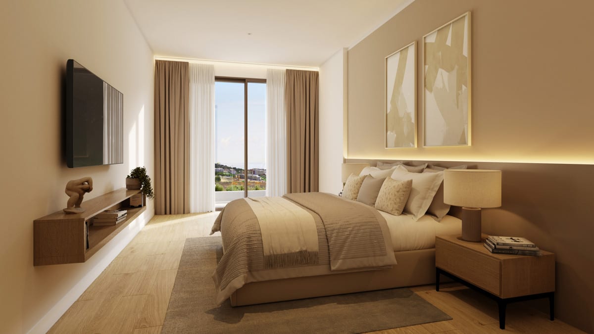 Rendered bedroom at KALA RESIDENCES with a double bed in beige tones, wooden bedside table with table lamp, wall-mounted television above a wooden cabinet and a large window with curtains.