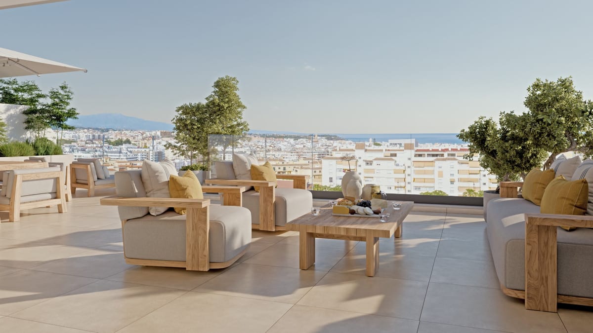 Project visualisation of LAS MESAS SEA SUITE with a spacious terrace, wooden lounge furniture with yellow cushions, a coffee table, glass balustrade and views over the town towards the sea on the horizon.