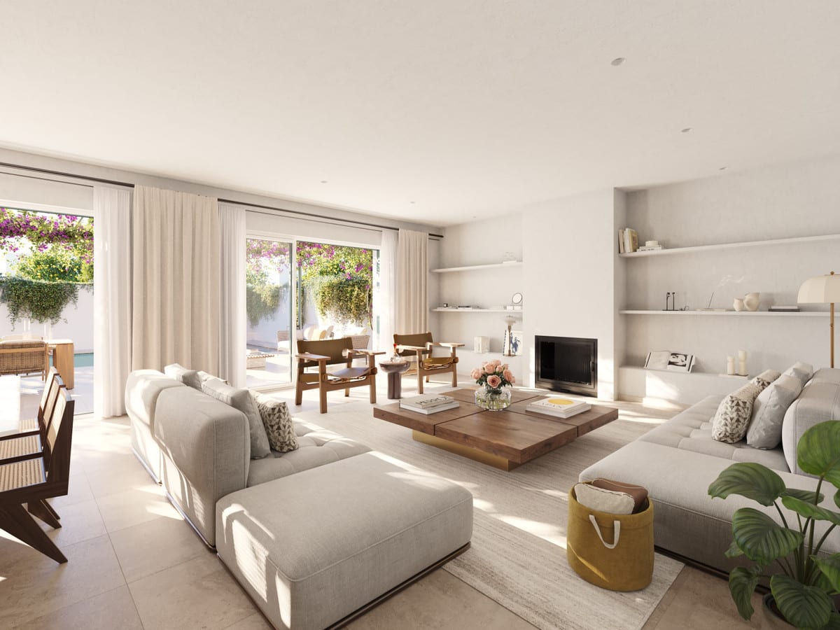 Project visualisation of LAS VILLAS–SOTOGRANDE featuring a living room, large light-coloured corner sofa, two wooden armchairs, wooden coffee table, fireplace and open sliding doors leading to a planted outdoor area.