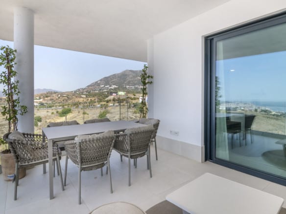 LOMAS 2: covered terrace with grey dining table, six woven chairs, glass balustrade and mountainous landscape.