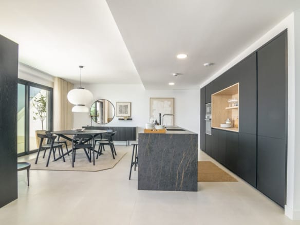 LOMAS 2: bright open-plan kitchen with dark cabinet wall, dark veined kitchen island and dining area by sliding glass doors.
