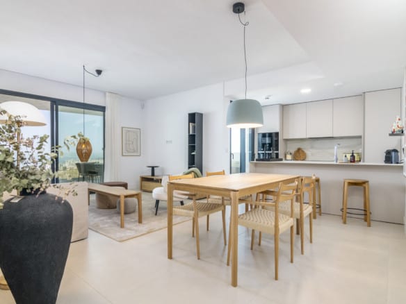 LOMAS 2: open-plan living space with wooden dining table, light kitchen, bar stools and seating area by sliding glass doors.