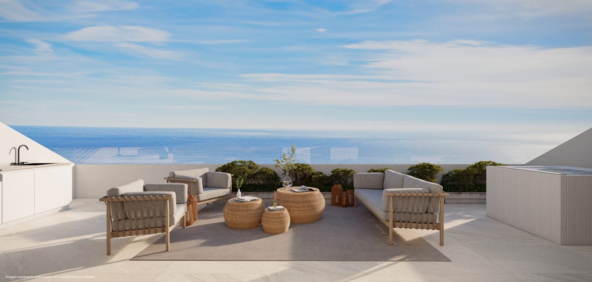 Project visualisation of the outdoor terrace at LOMAS UNIQUE A, with rattan lounge furniture, round woven coffee tables, an outdoor kitchen on the left, a low glass screen and sea views in the background.