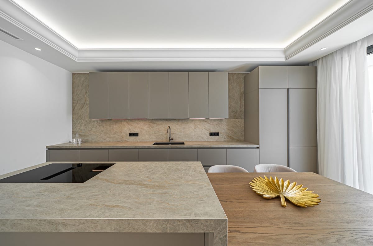 Kitchen island at LOMAS VILLAS with an integrated induction hob, taupe cabinetry, stone worktops and an adjoining wooden dining table.